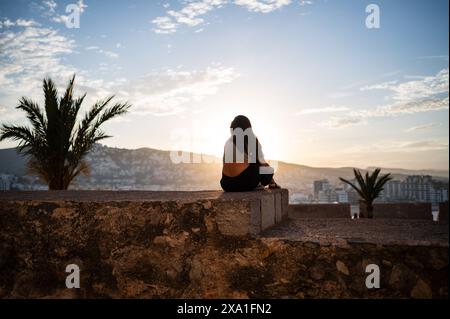 Junge Frau, die den Sonnenuntergang von den Stadtmauern des Schlosses Papa Luna in Peñiscola, Castellon, Valencianische Gemeinde, Spanien genießt Stockfoto