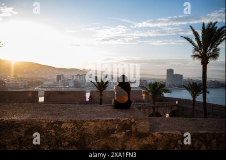 Junge Frau, die den Sonnenuntergang von den Stadtmauern des Schlosses Papa Luna in Peñiscola, Castellon, Valencianische Gemeinde, Spanien genießt Stockfoto