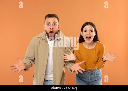 Junges Paar, das Überraschung und Aufregung gegen Orange ausdrückt Stockfoto