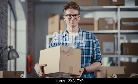 Porträt eines erfolgreichen Eigentümers eines kleinen Unternehmens, der lächelnd in die Kamera blickt. Kaukasischer Mann hält einen Karton in einem Lagerraum mit Bestellungen, die versandbereit sind. Stockfoto