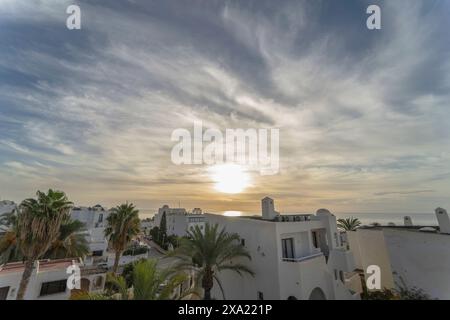 Ein beeindruckender Sonnenaufgang entfaltet sich über Mojacar, eingerahmt von Palmen und Gebäuden. Der Himmel, geschmückt mit hohen Zirruswolken, zeigt den Sonnenuntergang Stockfoto