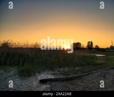 Ein Sonnenuntergang über dem Neusiedler See in Österreich, der Schilfgürtel und das Wasser in malerischen Farbtönen färbt Stockfoto