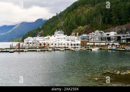 Zwei Fähren legten an einem Fährhafen an und warteten darauf, dass Passagiere und Fahrzeuge mit grünen Bergen im Hintergrund beladen wurden Stockfoto