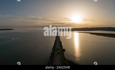 Ein malerischer Sonnenuntergang über einer gewundenen Straße am Wasser Stockfoto