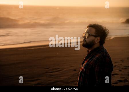 Ein Mann, der am Strand steht und den Sonnenuntergang beobachtet Stockfoto