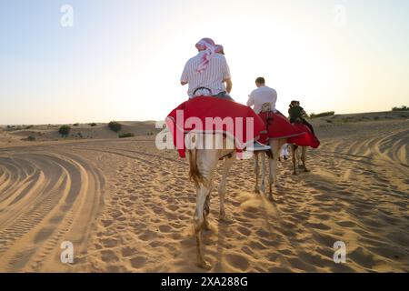 Gruppe von Einzelpersonen, die gemütlich auf Kamelen in der Sandwüste unter weichem Licht reiten Stockfoto