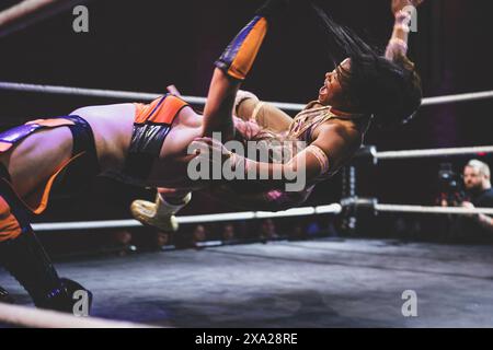 Eine Wrestlerin in orange und schwarz, die sich darauf vorbereitet, den Gegner zu treten Stockfoto