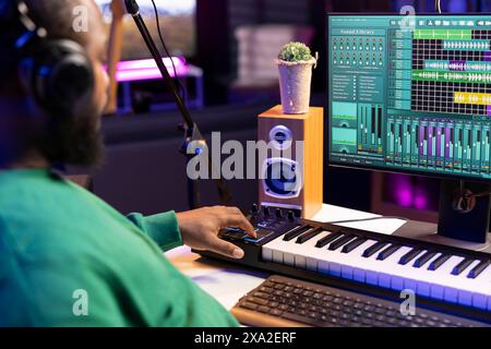 Musikingenieur fügt seinen Audiodateien im Heimstudio Synthesizer-Noten hinzu, bearbeitet Titel mit digitaler Software und produziert neue Songs für ein Album. Der Künstler arbeitet mit dem Mixen von Konsole und Ausrüstung. Stockfoto