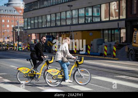 Paare überqueren Siltasaarenkatu mit HSL City Bikes oder Alepa Bikes im Bezirk Hakaniemi in Helsinki, Finnland Stockfoto