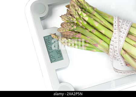 Ein Bündel frischer grüner Spargelspeere wird auf einer Glasskala platziert, die von einem weißen Maßband umgeben ist und Gesundheit und Ernährung symbolisiert. Stockfoto