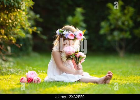 Kleines Mädchen mit Blumenstrauß im sonnigen Garten. Blühender Sommerpark. Kind mit Blumengeschenk für Geburtstagsfeier oder Osterfeier. Stockfoto