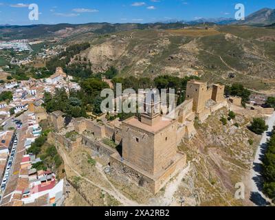 Historische Burganlage auf einem Hügel in einer bergigen Gegend Spaniens, umgeben von Vegetation bei sonnigem Wetter, Blick aus der Vogelperspektive, Festungsberg, Alcazaba Stockfoto