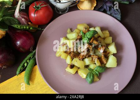 Eine Mahlzeit mit Kartoffelwürfeln und Pilzen, garniert mit Basilikum auf einem rosafarbenen Teller, umgeben von verschiedenen frischen Gemüsesorten Stockfoto