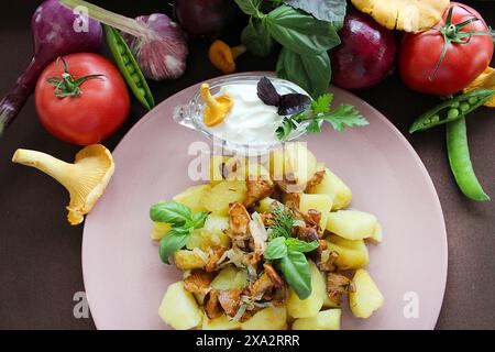 Ein Teller Kartoffeln gemischt mit Pilzen, garniert mit frischem Basilikum und Petersilie, umgeben von frischem Gemüse und einer Seite Sauerrahm Stockfoto