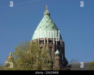 Der obere Teil eines Kirchturms mit einer grünlichen Kuppel und einem goldenen Kreuz, umgeben von Baumkronen, Haarlem, Niederlande Stockfoto