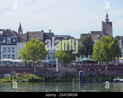 Straßen und Häuser einer Stadt mit Kirchturm und Bäumen am Ufer unter klarem Himmel, Maastricht, Niederlande Stockfoto