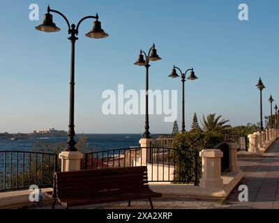 Promenade entlang des Meeres mit Bänken, dekorativen Lampen und Palmen, Geländer und klarem Himmel, Valetta, Malta Stockfoto