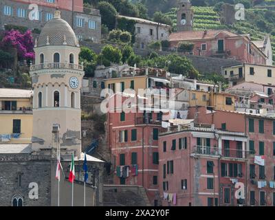 Ein malerisches Dorf mit bunten Häusern, einem Uhrenturm und Fahnen, eingebettet in eine üppige hügelige Landschaft, Bari, Italien Stockfoto