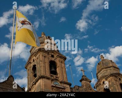 Historische Gebäude mit Türmen und einer winkenden Flagge vor einem blauen Himmel, Valetta, Malta Stockfoto