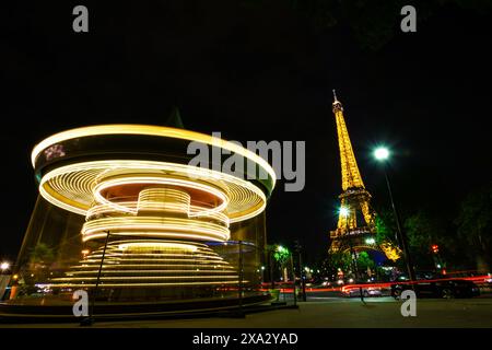 Nachtblick auf den Eiffelturm und das sich drehende Karussell in der Nähe in Langzeitbelichtung - Paris, Frankreich Stockfoto