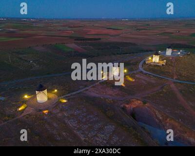 Nachtaufnahme mehrerer beleuchteter Windmühlen auf Hügeln in einer weiten Feldlandschaft bei Dämmerung, Luftaufnahme, Alcazar de San Juan, Ciudad Real, Castilla-La Stockfoto