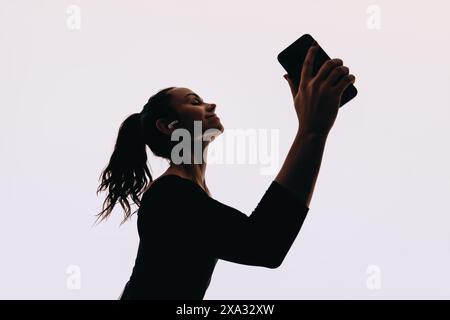 Frau tanzt mit ausdrucksstarken Bewegungen in einem Studio. Mit einem Smartphone und Ohrstöpseln hört sie gerne Musik. Eine Tänzerin zeigt sie Stockfoto