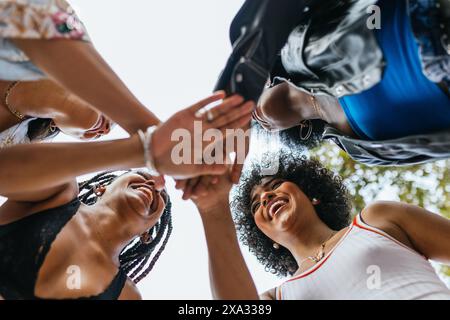 Eine Gruppe verschiedener weiblicher Freunde, die an einem sonnigen Tag draußen einen fröhlichen Handschlag teilen. Stockfoto
