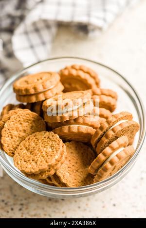 Ein Nahfoto einer Glasschale, gefüllt mit cremegefüllten Sandwichkeksen. Die Kekse werden nach dem Zufallsprinzip gestapelt und übereinander gelegt, und die Schüssel ist s Stockfoto