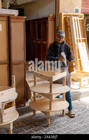 Taroudant, Marokko – 21. März 2024: Ein junger Zimmermann lächelt stolz und arbeitet in seiner Holzwerkstatt und klebt einen Stuhl Stockfoto