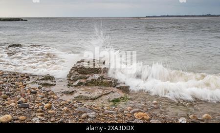 Wellen krachen über einen Kieselstrand, mit mehreren bunten Kieselsteinen an der Küste Stockfoto
