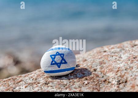 Israelische Flagge gemalt. Handgemalter Stein mit Magen David. Blaues Meer mit Wellen im Hintergrund Stockfoto