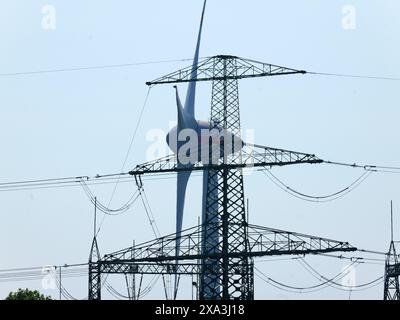 Ein Foto einer Windkraftanlage und eines Hochspannungsmastes symbolisiert die nachhaltige Energieerzeugung und den Übergang zu erneuerbaren Energiequellen. Stockfoto