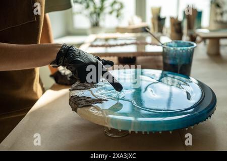 Nahaufnahme einer Künstlerin, die Epoxidharz mit Handschuhen aufträgt, in der Nahaufnahme des Kunststudios. Flüssige Kunst. Stockfoto