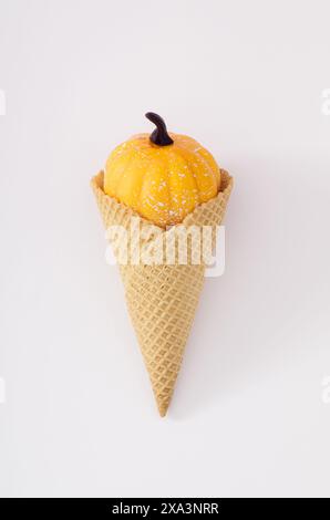 Kleiner Kürbis in Eiskegel auf weißem Hintergrund. Minimaler Hintergrund für Herbst- und Sommersaison. Eis mit Kürbis-Idee. Stockfoto