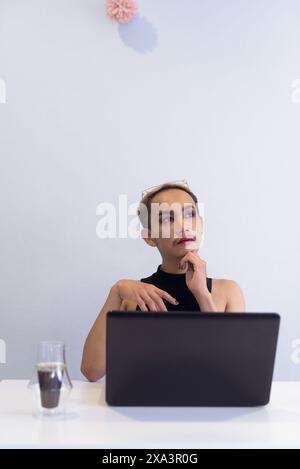 Porträt des schönen asiatischen queeren LGBT Community Unterstützers Mann mit Schnurrbart, der Lippenstift und Jumpsuit trägt und arbeitet und denkt im Büro, Kaffee und Stockfoto