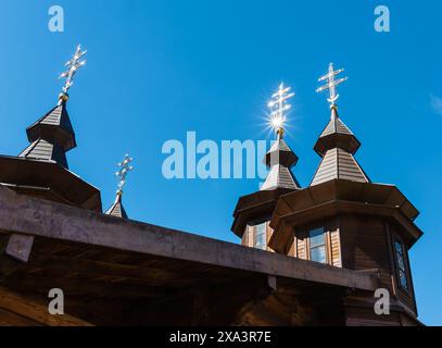 Lichtblitze von hellen Sonnensternen auf den goldenen Kreuzen einer hölzernen christlichen Kirche. Gegen den Himmel Stockfoto