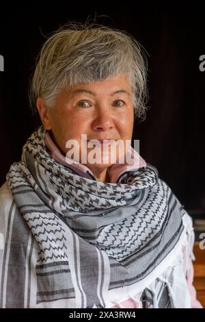 Eine ältere eurasische Chinesin/Italienerin, die einen Keffiyeh trägt, um ihre Unterstützung für Palästina zu demonstrieren Stockfoto