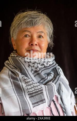 Eine ältere eurasische Chinesin/Italienerin, die einen Keffiyeh trägt, um ihre Unterstützung für Palästina zu demonstrieren Stockfoto