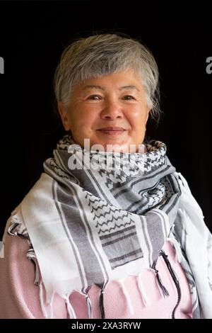 Eine ältere eurasische Chinesin/Italienerin, die einen Keffiyeh trägt, um ihre Unterstützung für Palästina zu demonstrieren Stockfoto