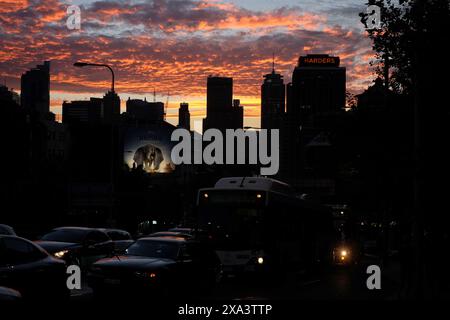 Silhouette der Skyline von Sydney mit rosa Wolken in der Abenddämmerung, vom Kings Cross aus gesehen, eine beleuchtete Plakatwand eines Elefanten in der Mitte links, Autos im Verkehr darunter Stockfoto