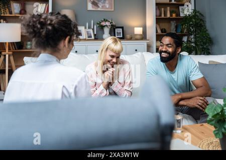 Zwei Leute, junge, vielfältige Paare, die versuchen, Probleme in ihrer Beziehung zu lösen. Multirassische Ehepartner lächeln, während sie sich vor einem Therapeuten in der Th unterhalten Stockfoto