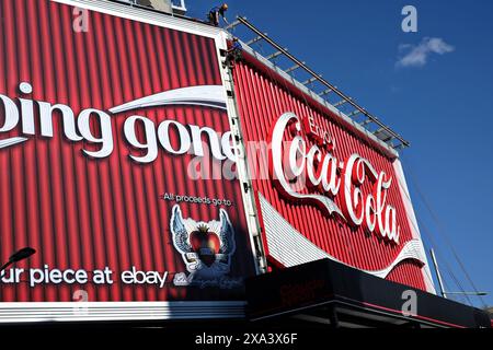 An einem sonnigen Tag, Kings Cross, schauten Arbeiter an, die über die Coca-Cola Neon-Reklametafeln wechselten Stockfoto