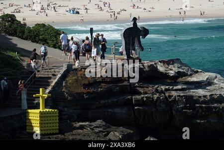 Skulptur am Meer, der felsige Spaziergang nach Bondi, eine gelbe Skulptur aus gesteckten Zylindern und ein 3D-Ausschnitt einer sich biegenden Person und ein Blick auf Bondi Beach Stockfoto