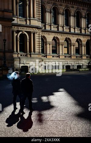 Zwei Männer, Silhouetten und Schatten, einer rauchend über den Rathausplatz durch einen Pool von hellem Morgenlicht an einem sonnigen Wintertag Stockfoto