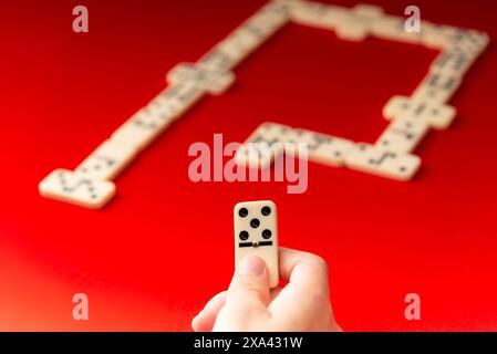 Domino-Spieler, der ein rechteckiges Acrylstück hält. Brettspiel. Roter Hintergrund. Stockfoto