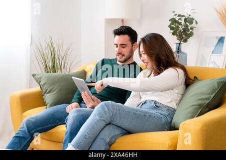 Ein Paar sitzt auf einem gelben Sofa mit einem Tablet Stockfoto