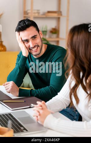 Mann in grünem Hemd lächelt Frau in der Nähe des Laptops an Stockfoto