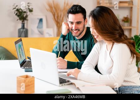 Zwei Leute lächeln und arbeiten an Laptops an einem Tisch. Stockfoto