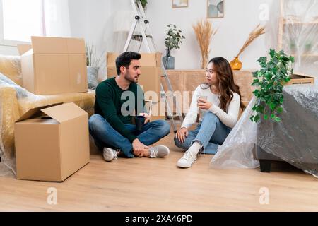 Ein Paar sitzt zwischen Umzugskästen in einem neuen Zuhause Stockfoto