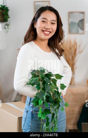 Lächelnde Frau, die drinnen eine Topfpflanze hält. Stockfoto